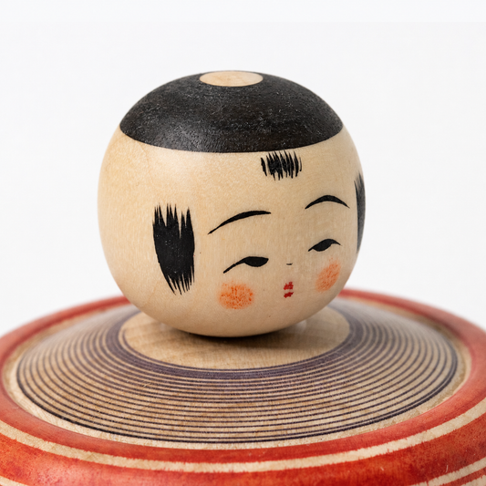Close-up of the red and indigo Bōzu Ejiko kokeshi, showing its painted face and wooden texture.