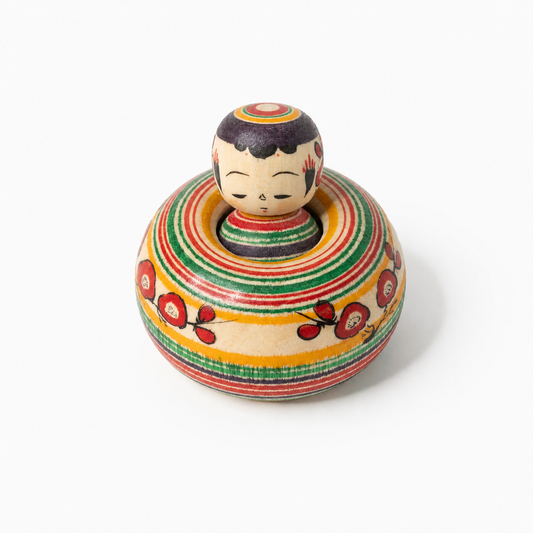 Ejiko-Kokeshi mit Pflaumenblüten und mehrfarbigen Ringen in Frontalansicht